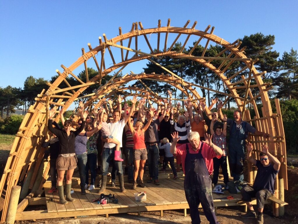 Onion Collective community building project. Lots of people  waving under a wooden arch.
