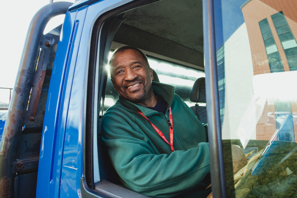 Senior truck driver is smiling while pulling out of a parking lot in his work truck.