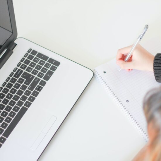laptop and woman making notes beside it