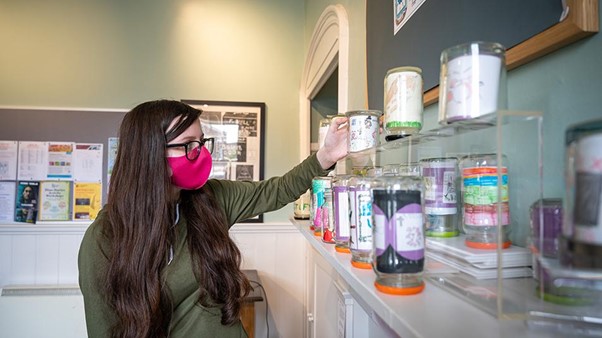 Young person wearing a mask standing in front of a row of jars. Getting work experience curating the 'Museum in a Jar' exhibition