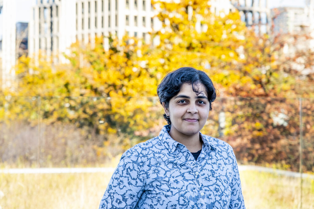 Waseem Meghjee standing outside with bright Autumnal leaves behind her.