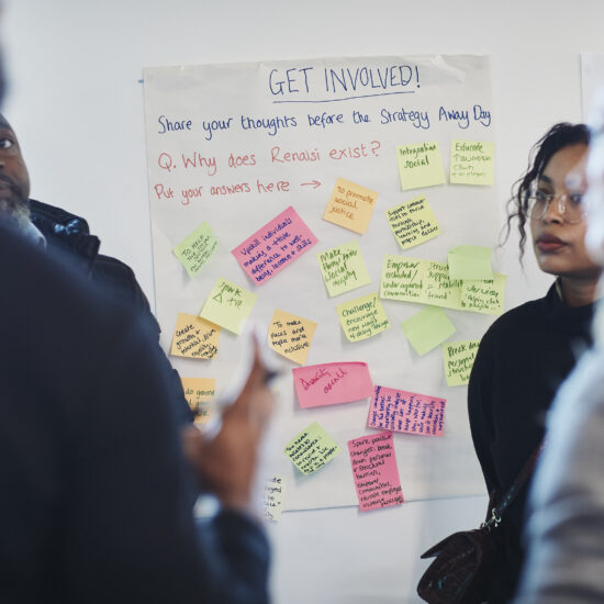 A group of Renaisi colleagues standing near a flipchart that reads "Why does Renaisi exist?" Answers on coloured post-it notes