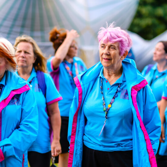 A group of Olympics volunteers wearing their blue jackets and lanyards. The woman at the front has pink hair.
