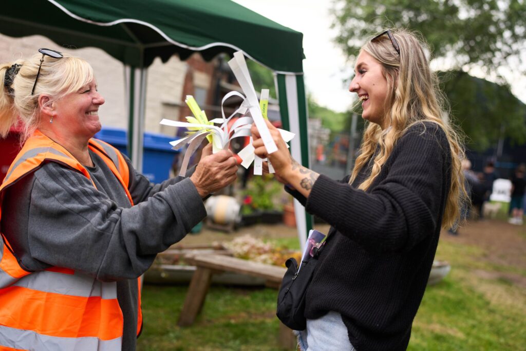 Two white women smiling and laughing at a festival, each holding a handful of wristbands.