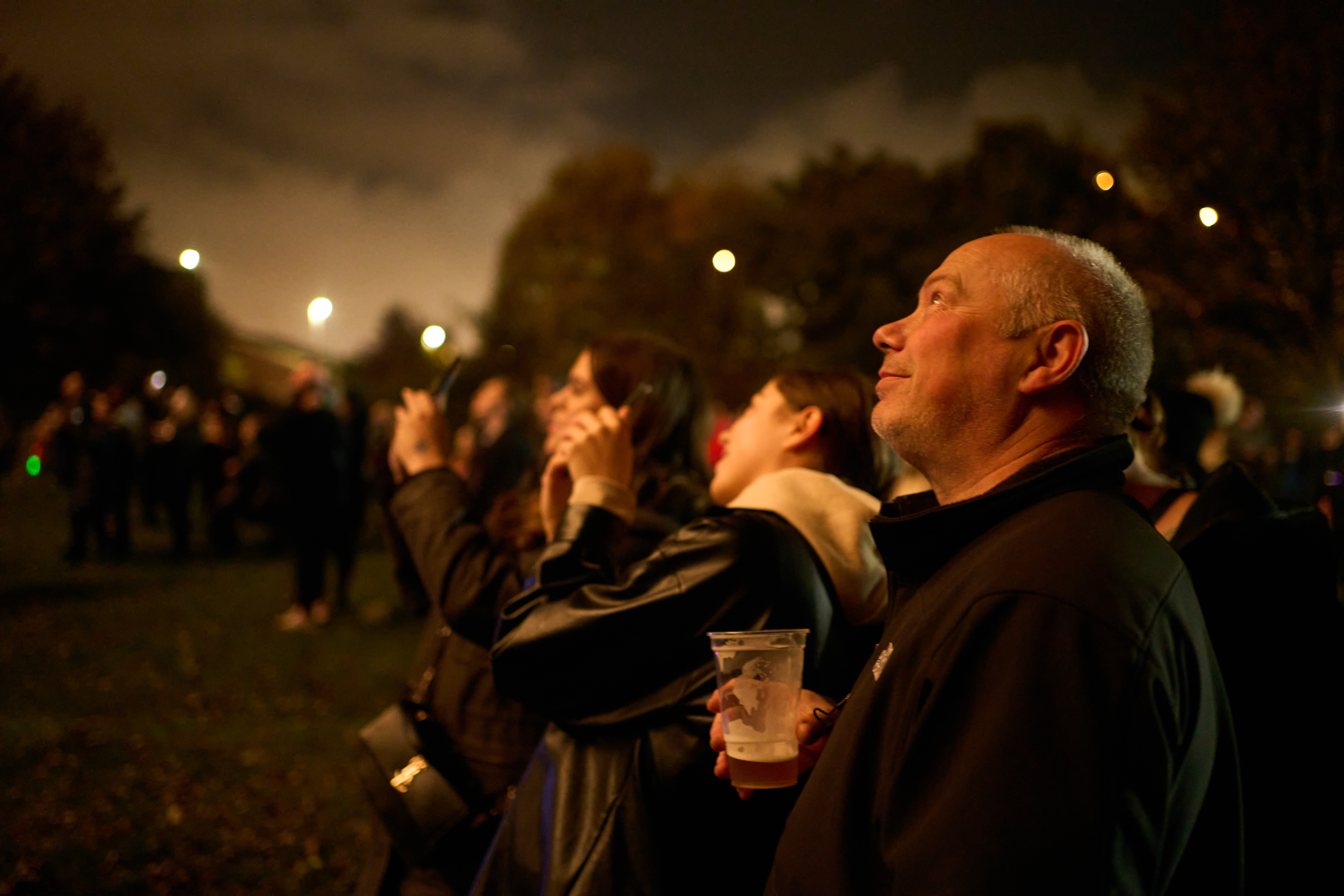 A man looking up at the night sky holding a beer.