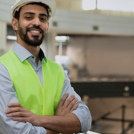 A bearded man wears a high vis jacket and white helmet. He's got his arms crossed and broad grin.